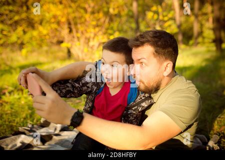 Selfie. Padre e figlio che camminano e si divertono nella foresta d'autunno, sembrano felici e sinceri. Laughting, giocare, avere buon tempo insieme. Concetto di famiglia, felicità, vacanze, infanzia, stile di vita. Foto Stock