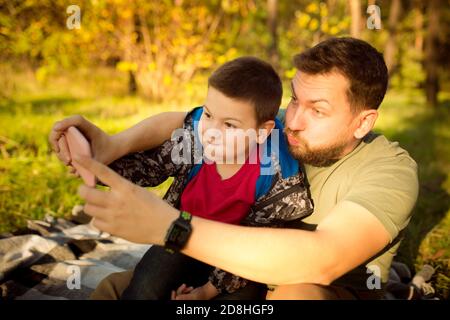 Selfie. Padre e figlio che camminano e si divertono nella foresta d'autunno, sembrano felici e sinceri. Laughting, giocare, avere buon tempo insieme. Concetto di famiglia, felicità, vacanze, infanzia, stile di vita. Foto Stock