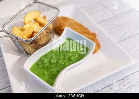 Cena a base di pesce, patatine e piselli moschi servita su un piatto quadrato visto dall'alto. Una cena tradizionale inglese spesso il venerdì. Foto Stock