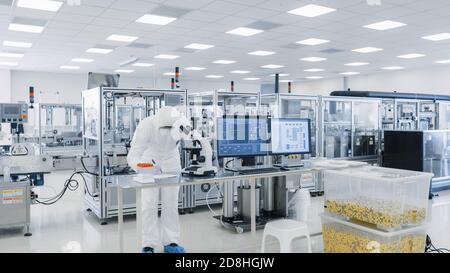 Shot of Sterile High Precision Manufacturing Laboratory dove gli scienziati della tuta protettiva utilizzano computer e microscopi, facendo prodotti farmaceutici Foto Stock