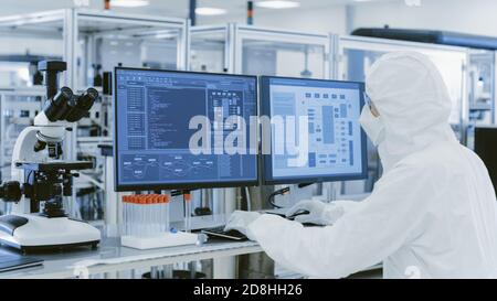 In laboratorio sopra la vista della spalla dello scienziato in vestiti protettivi che fanno la ricerca su un personal computer. Produzione manufattura moderna Foto Stock