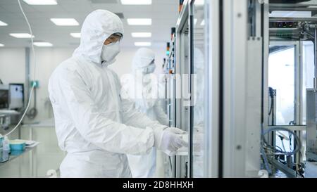 Nell'impianto di produzione Team di scienziato che indossa tuta protettiva sterile Set's up Programs Modern Industrial 3D Printer, High Precision Foto Stock
