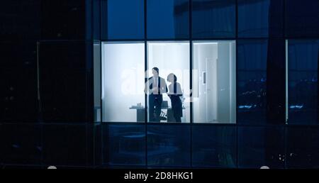Foto aerea dall'esterno dello Skyscraper: Uomo d'affari e donna d'affari che parlano mentre si guarda fuori dalla finestra dell'ufficio. Shot of the Business Foto Stock
