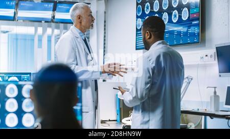 Il team di scienziati lavora nel Brain Research Laboratory, discutendo Brain Scans Show su Wall TV Monitor. Neurologi neuroscienziati Foto Stock