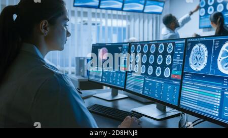 Over the Shoulder Shot of Female Medical Scientist lavorare con immagini TAC Brain Scan su un personal computer in laboratorio. Neurologi in Ricerca Foto Stock