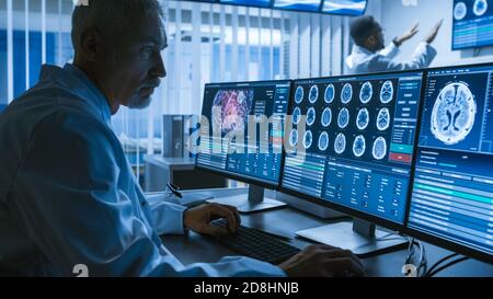 Over the Shoulder Shot di Senior Medical Scientist che lavora con immagini TAC Brain Scan su un personal computer in laboratorio. Neurologi in Ricerca Foto Stock