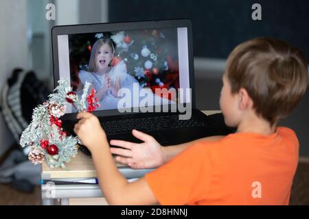 Il bambino è seduto su un computer portatile e parla con un amico tramite collegamento video. Soggiorno a casa, quarantena e divaricamento sociale durante i nuovi anni. Foto Stock