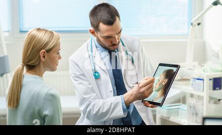 Il chirurgo cosmetico di plastica consulta la donna circa chirurgia dell'ascensore facciale, disegna le frecce sullo schermo del calcolatore del Tablet digitale, mostrando i tipi di lifting e. Foto Stock