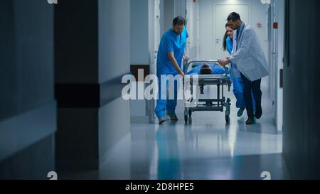 Pronto soccorso: Medici, infermieri e paramedici spingere Gurney Stretcher con il paziente gravemente ferito verso la sala operatoria. Moderno e luminoso Foto Stock