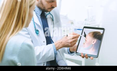 Il chirurgo cosmetico di plastica consulta la donna circa Chirurgia dell'elevatore facciale, punta allo schermo del calcolatore del Tablet digitale che mostra i tipi di lifting, fronte Foto Stock