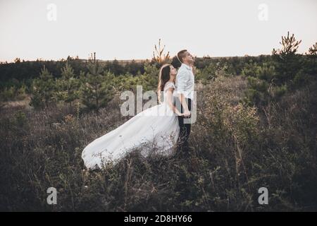 sposa e sposo che camminano sul prato in estate a. tramonto Foto Stock