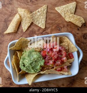 Nachos con guacamole all'avocado e salsa, serviti in una ciotola bianca su un piatto di legno. Foto Stock
