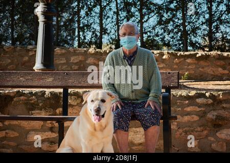 Nonna con il suo animale domestico è seduta su una panchina con la sua maschera Foto Stock