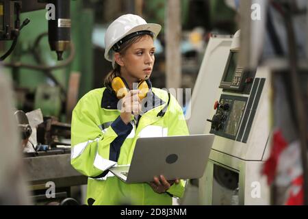 Operatrice di tecnici in uniforme che lavora su un computer portatile con una macchina in produzione. Foto Stock