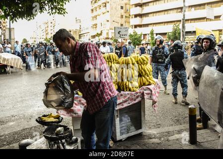 Beirut, Libano, 30 ottobre 2020. Un uomo continua a vendere banane mentre la polizia lo circonda durante gli scontri tra un piccolo gruppo di uomini di Tripoli e Beirut e le forze libanesi di sicurezza interna. Scuffi sono scoppiati durante un tentativo del gruppo panislamico Hizb Ut Tahrir di marciare all'ambasciata francese per protestare contro ciò che essi hanno visto come la posizione anti-islamica del presidente Emmanuel Macron. Le emozioni hanno corso alto come è stato sentito il profeta Maometto è stato disrispettato durante il suo mese di compleanno. Credit: Elizabeth Fitt/Alamy Live News Foto Stock