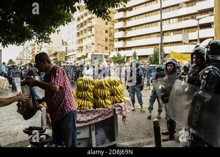 Beirut, Libano, 30 ottobre 2020. Un uomo continua a vendere banane mentre la polizia lo circonda durante gli scontri tra un piccolo gruppo di uomini di Tripoli e Beirut e le forze libanesi di sicurezza interna. Scuffi sono scoppiati durante un tentativo del gruppo panislamico Hizb Ut Tahrir di marciare all'ambasciata francese per protestare contro ciò che essi hanno visto come la posizione anti-islamica del presidente Emmanuel Macron. Le emozioni hanno corso alto come è stato sentito il profeta Maometto è stato disrispettato durante il suo mese di compleanno. Credit: Elizabeth Fitt/Alamy Live News Foto Stock