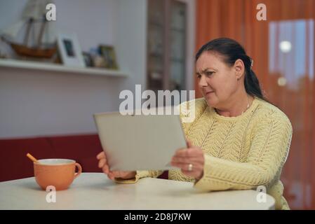 Donna anziana in giallo maglione cercando notebook con viso infelice Foto Stock