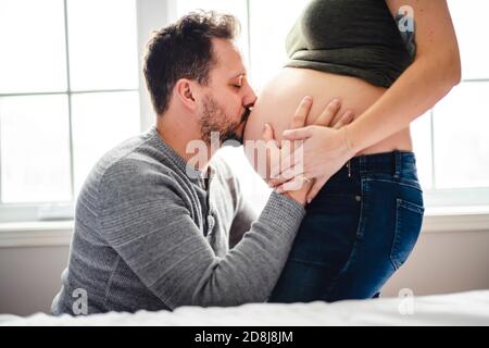 Felice giovane uomo bacio al ventre incinta delle donne Foto Stock