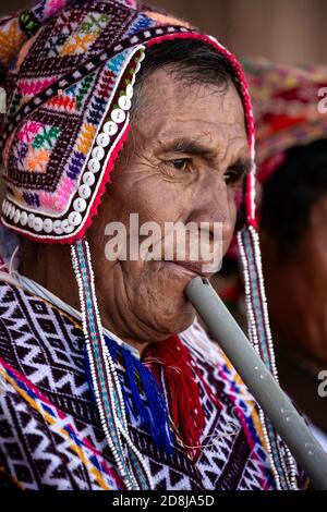 Quechua uomo indossando costume tradizionale (compreso il chullo) e suonando flauto, Pisac Domenica mercato, Pisac, Perù Foto Stock