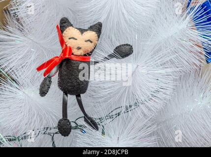 Giocattolo fatto a mano sotto forma di gatto sullo sfondo di un albero di Natale bianco. Capodanno e Natale decorazione Foto Stock