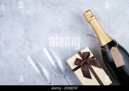 Sfondo natalizio con una bottiglia di champagne, bicchieri da vino e una scatola regalo su sfondo grigio. Foto Stock