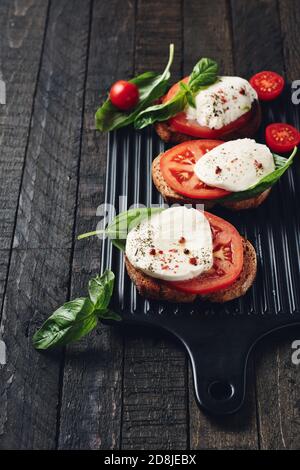 Panini aperti o bruschetta con mozzarella, pomodori e basilico, caprese su sfondo di legno scuro. Foto Stock