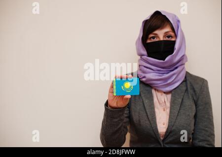 Ritratto di giovane donna musulmana che indossa abiti formali, proteggi maschera facciale e sciarpa testa hijab, tieni carta bandiera Kazakhstan contro sfondo isolato. Cor Foto Stock