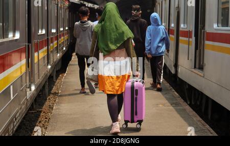 Giacarta / Indonesia - 23 settembre 2020. Una donna in una felpa con cappuccio verde sta trascinando la valigia rosa da un treno elettrico. Foto Stock