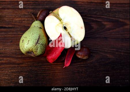 Decorazioni autunnali, foglie rosse, pera, mela e castagne su tavola di legno Foto Stock