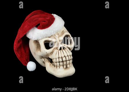 Cranio di Halloween che indossa il cappello di Natale di Babbo Natale isolato su nero Foto Stock