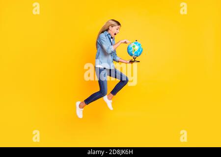 Foto di dimensioni del corpo di lunghezza intera di salto alto schoolgirl stupito mantenere il globo puntato sul continente gridando stupito isolato su luminoso colore giallo Foto Stock