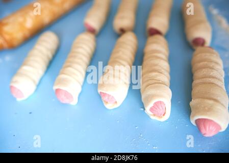 Sbozzati per torte fritte. Le salsicce sono avvolte in sottili strisce di impasto di lievito. L'impasto si sta alzando. Messa a fuoco selettiva Foto Stock