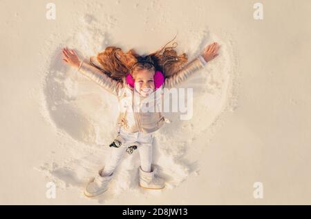 Angelo di neve fatto da un bambino nella neve. Bambino sorridente sdraiato sulla neve con spazio per la copia. Capretto divertente che fa l'angelo della neve. Foto Stock