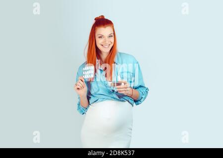 Non dimenticate le vostre pillole, vitamine, minerali, supliments. Meraviglioso modello giovane con un bicchiere d'acqua e pillole per incinta sorridente a macchina fotografica Foto Stock