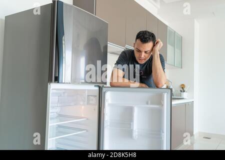 Il ragazzo è triste vicino al frigorifero vuoto senza cibo. Pubblicità del servizio di consegna del cibo. Foto Stock