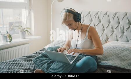 Giovane donna che usa il computer portatile in camera da letto. Freelance che lavora dalla comodità della sua casa. Foto di alta qualità Foto Stock