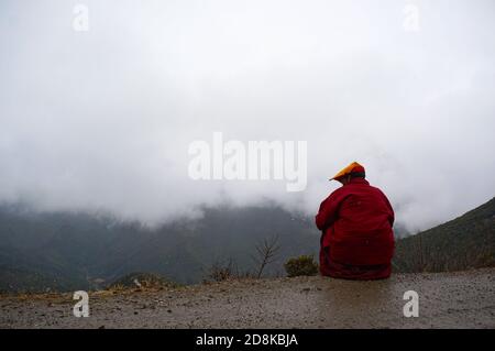 Monaco tibetiano in rosso accappatoio seduto sulla strada dentro le montagne Foto Stock