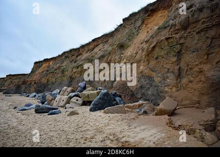 Le scogliere di Happisburgh Beach che mostrano erosione costiera, Norfolk, Regno Unito. Grandi massi sono lungo la base della scogliera per rallentare e prevenire l'erosione. Foto Stock