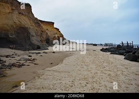 Le scogliere di Happisburgh Beach che mostrano erosione costiera, Norfolk, Regno Unito. Le antiche difese marine in legno sono visibili lungo il bordo della spiaggia. Foto Stock