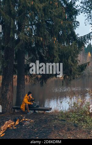Un uomo si siede sul lago su una panchina, accanto ad un albero. Foto Stock