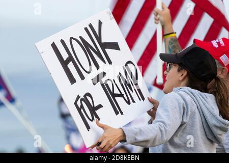 Chi sventola un cartello "HONK FOR TRUMP" al passaggio di auto e camion in un rally locale sul marciapiede. Foto Stock