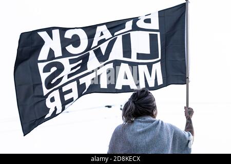 La persona tiene una bandiera grande 'BLACK LIVES MATTER' in testa al rally locale del marciapiede. Foto Stock