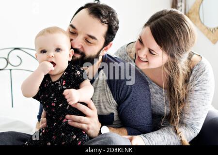 Happy family, mother, father and baby on the white bed Stock Photo