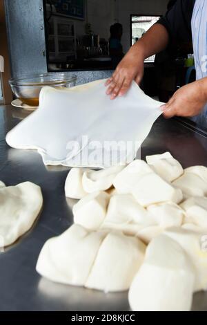 Primo piano di mani femminili che impastano l'impasto di Roti con olio sul tavolo in acciaio inox. Sfocatura del movimento. Foto Stock