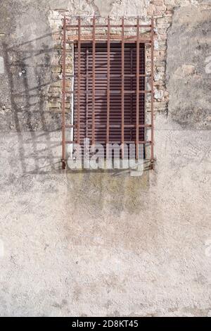 Particolare di ombra gettata sul muro dalla ruggine grattugiata di una vecchia finestra di casa nel borgo medievale in cima alla collina, girato in luce intensa a San Gimignano, Siena, Toscana, Foto Stock