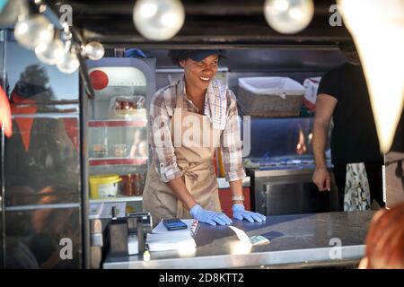 giovane amichevole afroamericana dipendente femminile in strada fast food servizio, alimentari camion concet Foto Stock