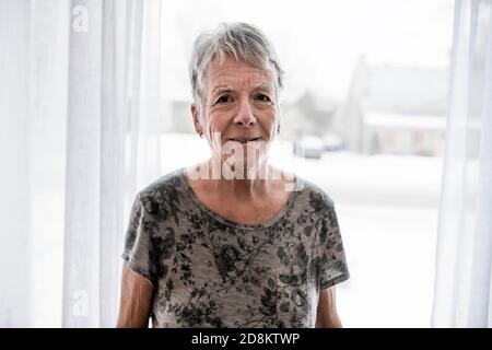 Donna anziana triste a casa vicino alla finestra Foto Stock