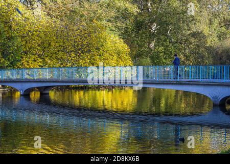 Scena autunnale. Cambia colore a St. James Park, Londra. Uomo irriconoscibile che cammina sul ponte. Foto Stock