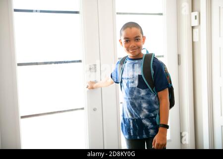 Un bambino che viene a casa passando attraverso la porta dopo scuola Foto Stock