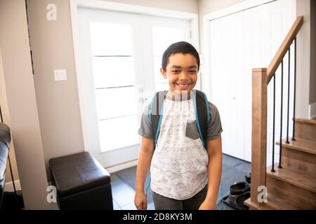 Un bambino che viene a casa passando attraverso la porta dopo scuola Foto Stock